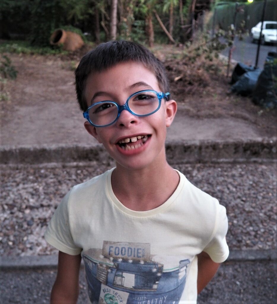 Child smiling outdoors in blue glasses