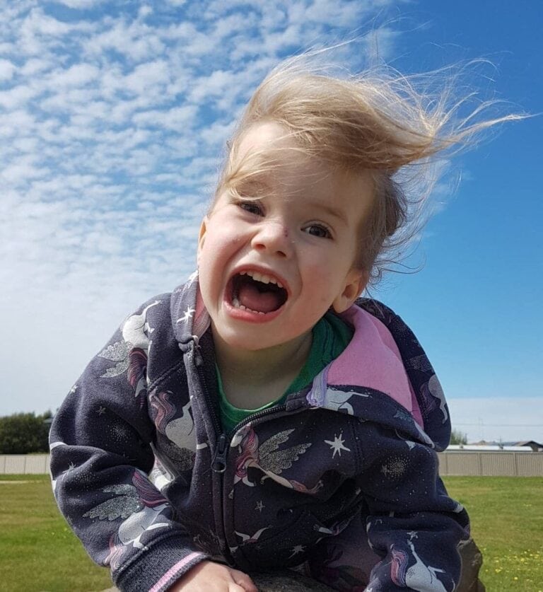 Child smiling outside under a bright sky